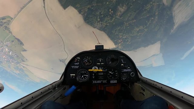 looping in a sailplane, stopping in mid air and then flying down headfirst above fields and forests, pilot's point of view from a cockpit