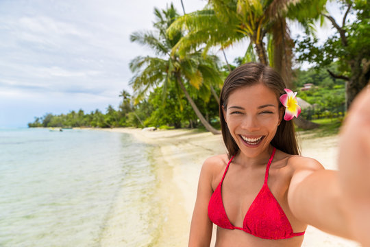 Beach vacation selfie bikini woman happy smiling. Asian girl holding cellphone taking photo with phone camera. taking holiday memories with smartphone pictures app. Tropical summer destination.