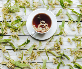 Herbal medicine. White cup of linden tea on linden blossom background. Top view. Treatment of cold and flu concept.