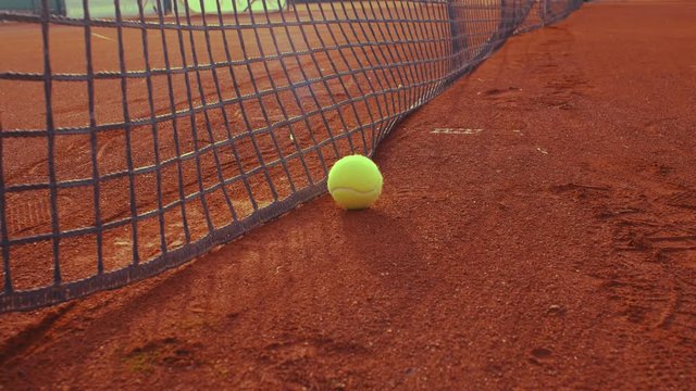 Rolling tennis ball on clay  tennis court and stop in the net, 4k, slow motion 75fps