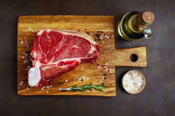 Raw meat steak with seasoning on a cutting board, background concrete. . Beef T-bone steak, top...