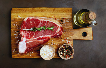 Raw meat steak with seasoning on a cutting board, background concrete. . Beef T-bone steak, top...