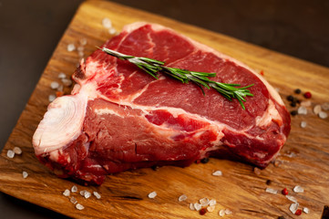Raw meat steak with seasoning on a cutting board, background concrete. . Beef T-bone steak, top view. Barbecue concept. Ingredients for roasting meat.