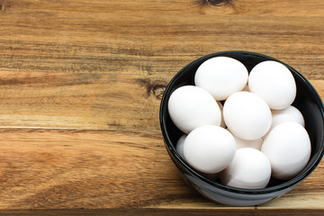 Black bowl with white eggs standing on the wooden table