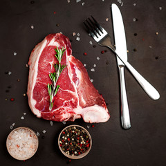Raw meat steak with seasoning on concrete background. Beef T-bone steak, top view. Barbecue...