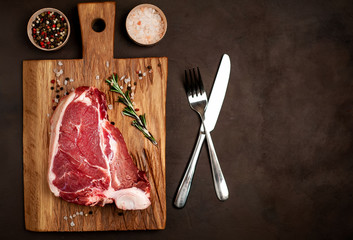 Raw meat steak with seasoning on a cutting board, background concrete. Space for text. Beef T-bone...