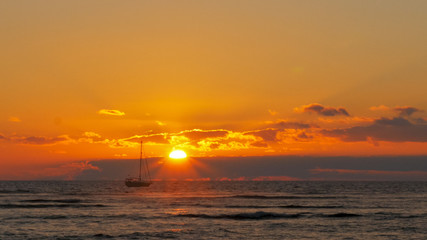 Fototapeta na wymiar yacht sails past the setting sun at waikiki