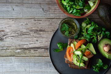Healthy avocado sandwich on dark rye toast bread made with fresh sliced avocado, seeds and tomatoes on rustic wooden background. Copy space.