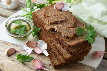 Sliced wholegrain bread wit seeds, greens, oil and garlic on cutting board. Carbohydrates.