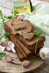 Sliced wholegrain bread wit seeds, greens, oil and garlic on cutting board. Carbohydrates.