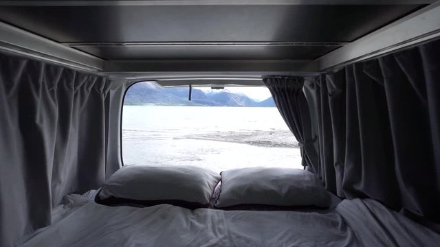 Interior of motorhome bed with pillows and blankets by Lake Wakatipu, Queenstown, New Zealand with snowcapped mountains in background