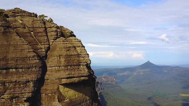 Drone circling cliff face revealing mountains and rocky escarpments in the background. Location NSW, Australia.