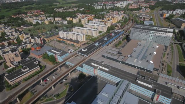 Aerial view of the KTH Royal Institute of Technology campus in Kista. A bright blue train of the public transportation system entering the passenger station. Colorful modern university buildings.