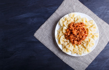 Farfalle bolognese pasta with minced meat on black wooden background.