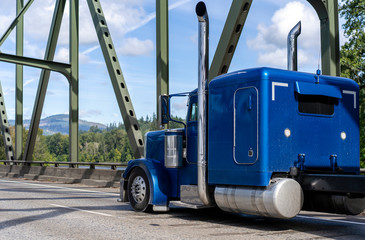 Bright blue classic American idol big rig bonnet semi truck tractor running on the arched truss...
