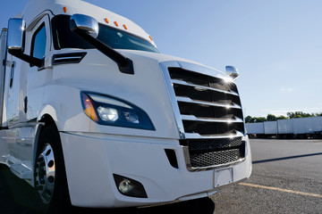 Bright white stylish big rig semi truck standing on truck stop at sunshine time