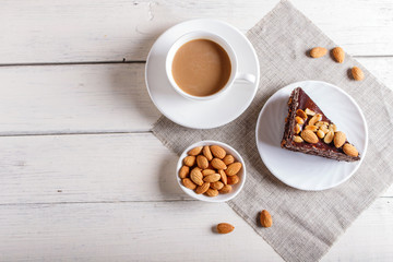 Chocolate cake with caramel, peanuts and almonds on a white wooden background.