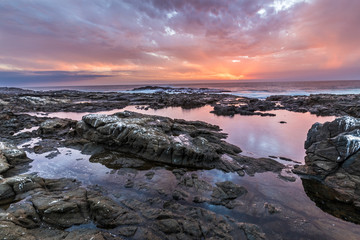 Sunset at Anzota Caves seafront walk. The rays of light coming from the sun illuminating the clouds and with amazing reflections over the Pacific Ocean sea waters while the waves moves over the rocks