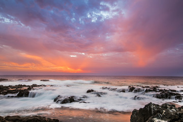 Obraz premium Sunset at Anzota Caves seafront walk. The rays of light coming from the sun illuminating the clouds and with amazing reflections over the Pacific Ocean sea waters while the waves moves over the rocks