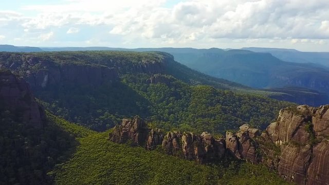 Drone turning in an arc revealing large rock structure and cliffs with mountains in the background.