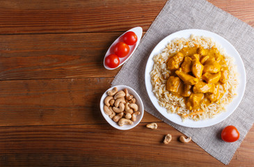 Rice with chicken curry sauce with cashew on brown wooden background.