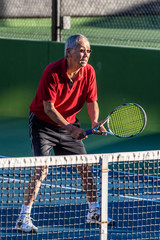 Focused Chinese elderly man ready with racquet raised during a game of tennis.