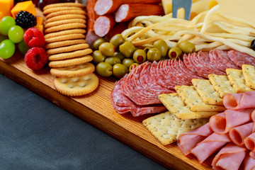 Closeup of cutting board with sliced salami, crackers, green olives, nuts and berries and assorted cheese.