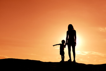 Fototapeta na wymiar Silhouette mother and daughter on the mound at the sky sunset.