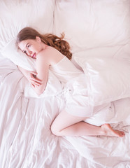 Beautiful young and happy woman sleeping while lying in white bed comfortably. Lonely girl in bed missing her partner overhead view of sleeping beauty.