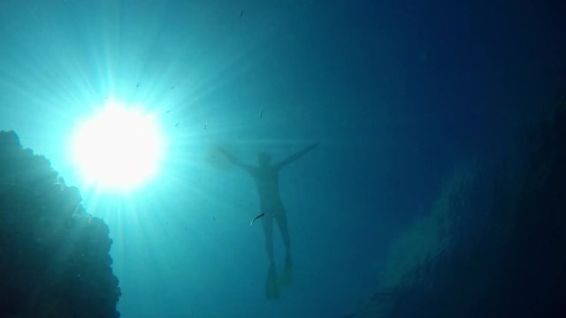 Freediver slowly descending from surface to bottom of Lake Ohrid in Macedonia in very clear and transparent water. Shot from bottom with view of sun.
