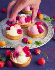 Cakes with strawberries and berries. Raspberry tarts on dark background. Hand takes cake from Vintage Plate.