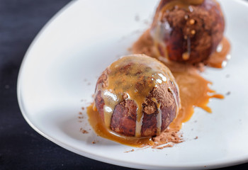 Energy balls cakes with chocolate and caramel on white plate on black background.