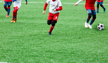 Boys in red and white sportswear plays soccer on green grass field. Youth football game. Children sport competition, kids plays outdoor,  activities, training
