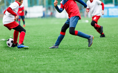 Boys in red and white sportswear plays soccer on green grass field. Youth football game. Children sport competition, kids plays outdoor,  activities, training