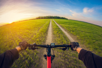 Riding bike on dirt road in field at sunset, first-person view, distortion perspective fisheye lens