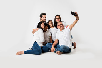 Indian family taking selfie picture with smartphone while sitting on white background includes 3...
