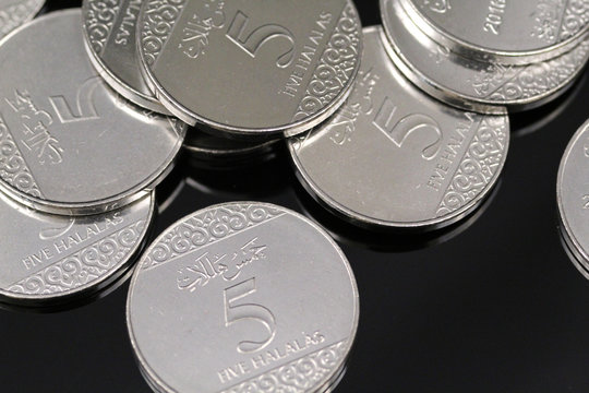 A pile of shiny new five halala coins in macro on a reflective black background