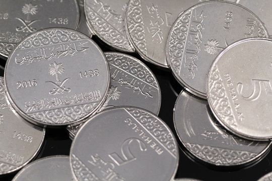 A pile of shiny new five halala coins in macro on a reflective black background