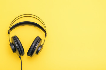 Black headphones with wires on a yellow background.