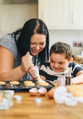 Obraz na płótnie Canvas Mother helping son to put frosting onto cupcakes