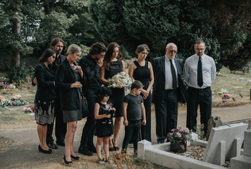 Family giving their last goodbyes at the cemetery - obrazy, fototapety, plakaty