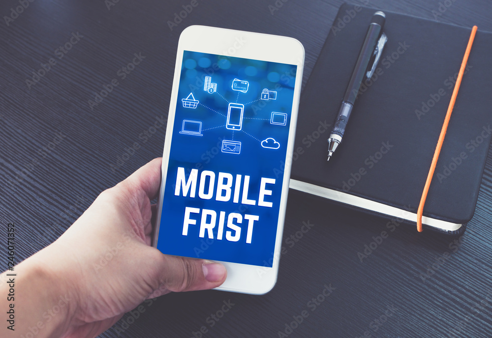Poster hand holding mobile phone with mobile first word and feature icon over notebook on black wood table 