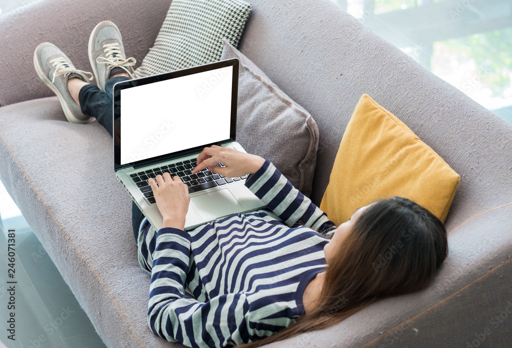 Poster Asian Woman in casual cloth lying down on sofa and using laptop computer with blank screen,Mock up for display or montage of your design,Clipping path on screen,Modern digital lifestyle..