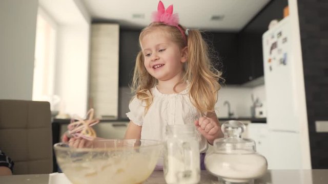 A Little Girl Is At The Kitchen. She Is Trying To Cook Something. She Is Whipping Cream With A Whisk. But Than Whisk Falls From Her Hands On Table And Girl's Mom Clean Her Hand From A Cream.