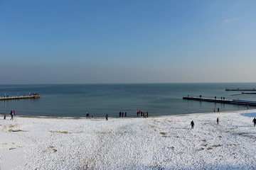 Snow-covered beach, sunny day. Sea in the city, walking to the beach