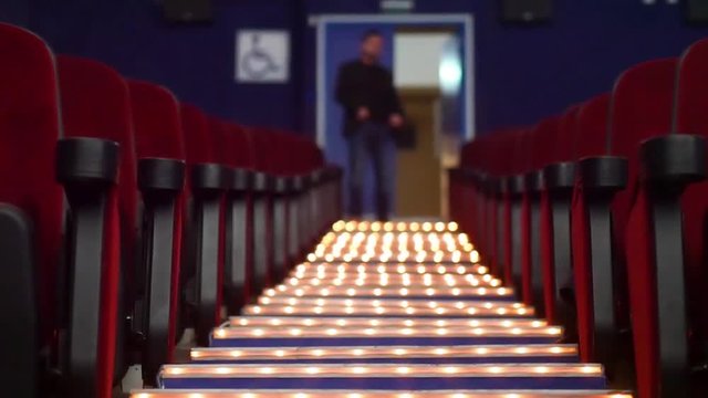 A blurred man walks down the center aisle of an empty movie theatere in slow motion