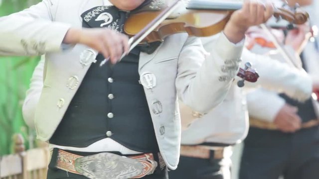 three mexican mariachis with white mariachi costume playing the violin at a mexican party