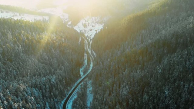 Wonderful sunlight over mountains covered with winter forest. Drone view of the road in the beautiful hills in the countryside from above.