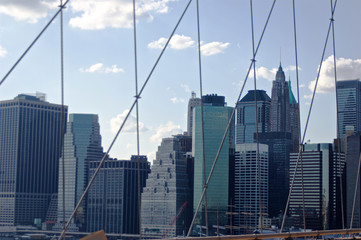 Fototapeta na wymiar A cluster of buildings situated in New York City's lower Manhattan as seen through the high-tension wires of the iconic Brooklyn Bridge.