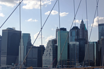 A cluster of buildings situated in New York City's lower Manhattan as seen through the high-tension wires of the iconic Brooklyn Bridge.